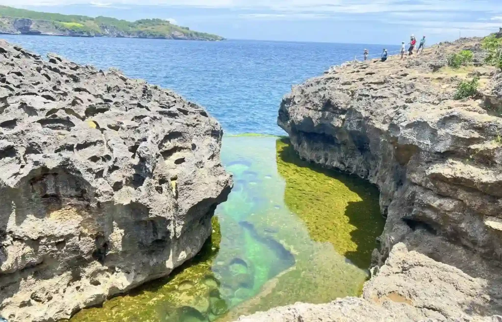 Piscina natural entre acantilados rocosos con mar abierto.