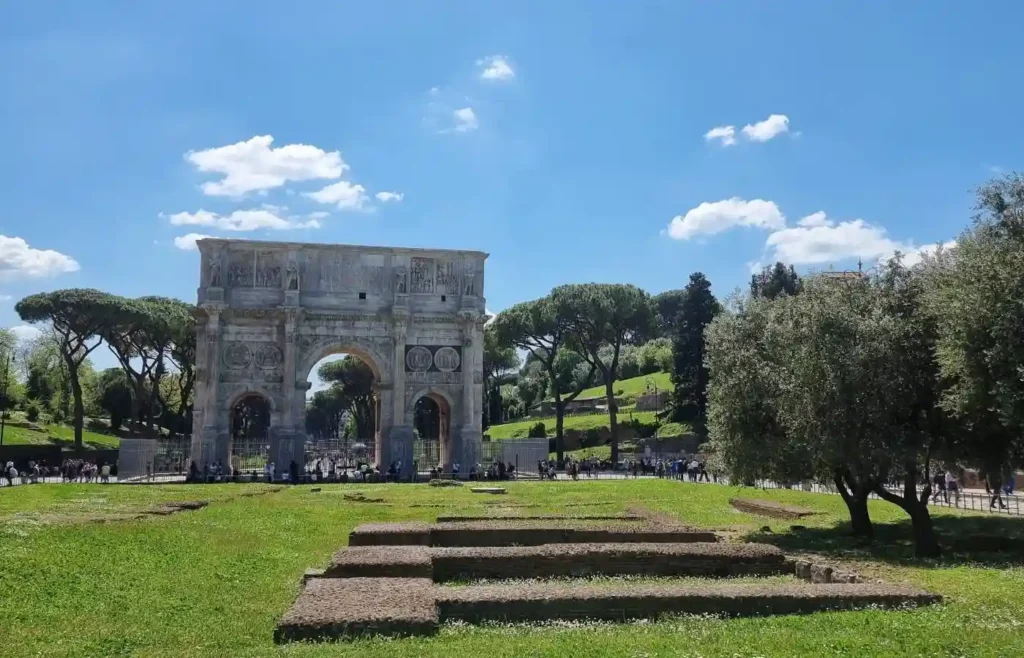 El histórico Arco de Constantino rodeado de zonas verdes y árboles bajo el cielo de Roma.