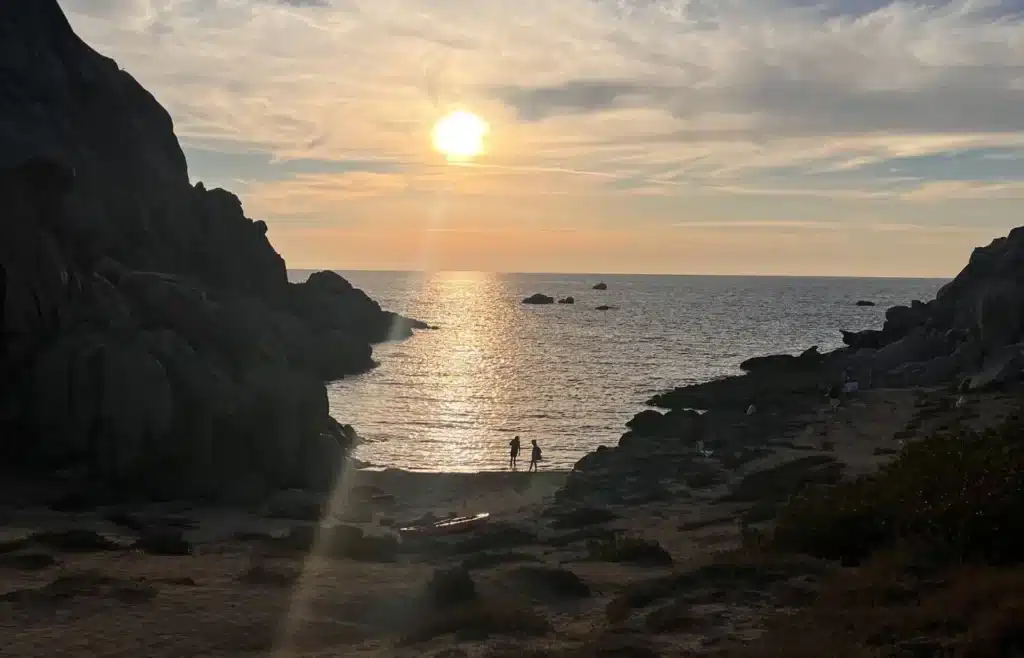 Atardecer dorado sobre el mar entre rocas con figuras.