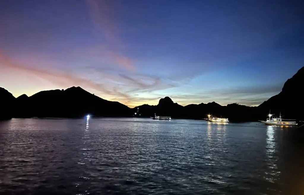 Atardecer vibrante sobre el mar con montañas y barcos iluminados.