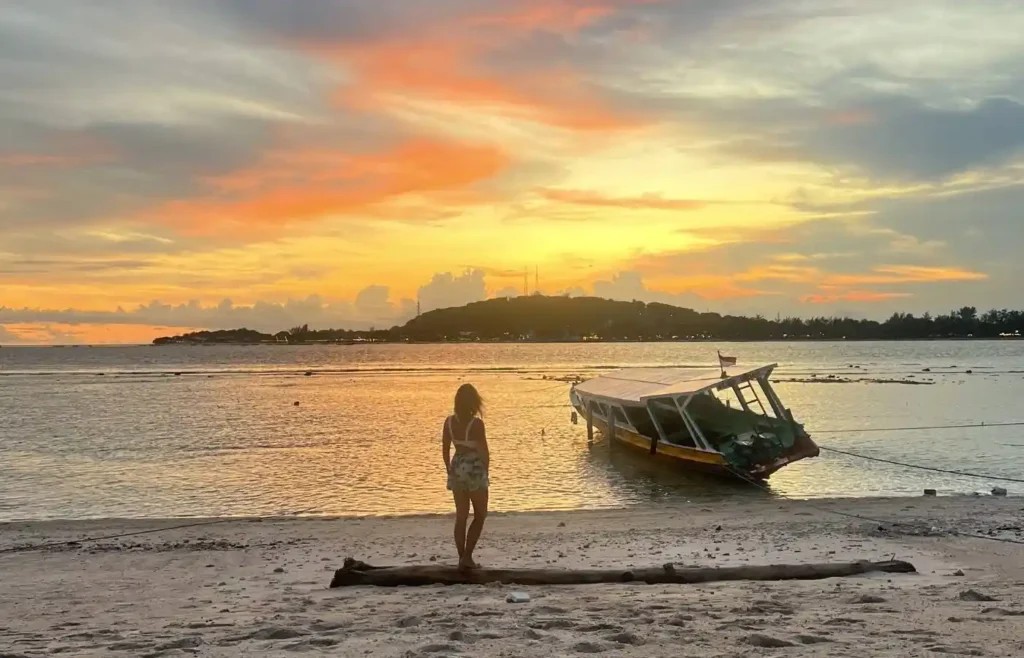 Atardecer tropical con mujer en playa y barco varado.