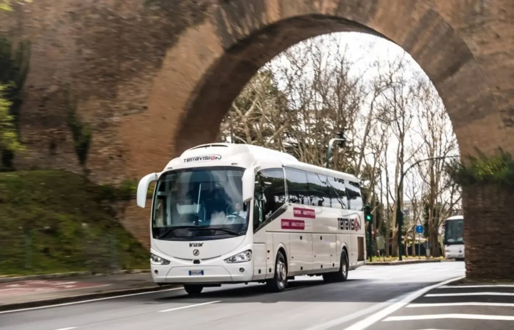 Autobús de traslado de pasajeros circulando junto a una muralla histórica en el centro de Roma.