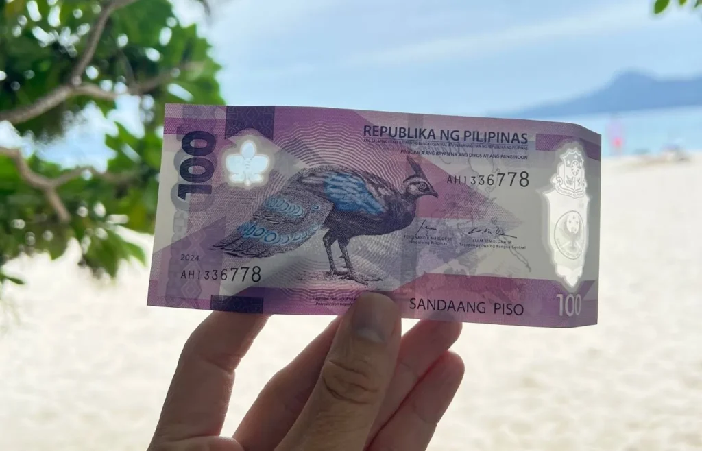 Mano sujetando un billete de 100 pesos filipinos en una playa de Filipinas.