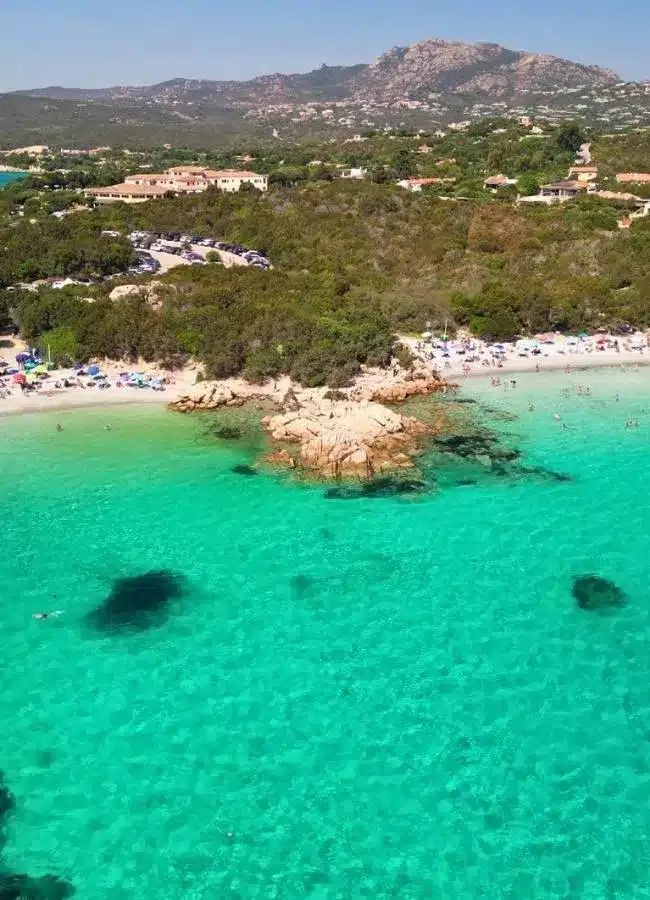 Fotografía aérea de dron de una cala de agua esmeralda rodeada de vegetación mediterránea en Cerdeña.
