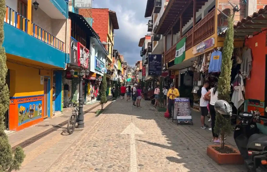 Calle peatonal colorida con tiendas, gente y adoquines.