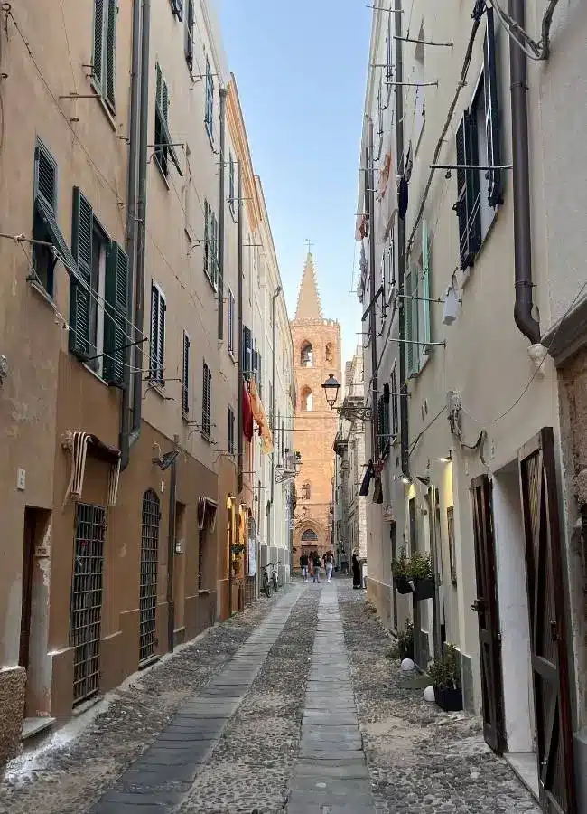 Callejuela estrecha tradicional del casco antiguo de Alguero con el campanario al fondo.