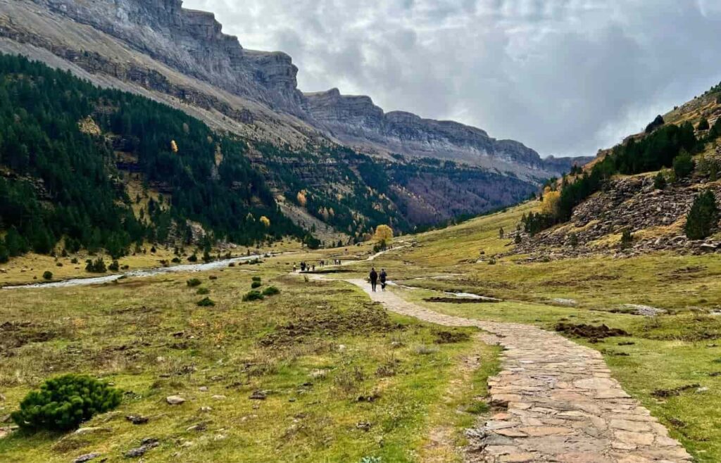 Sendero empedrado que recorre la pradera de Ordesa con las montañas al fondo bajo un cielo nublado.