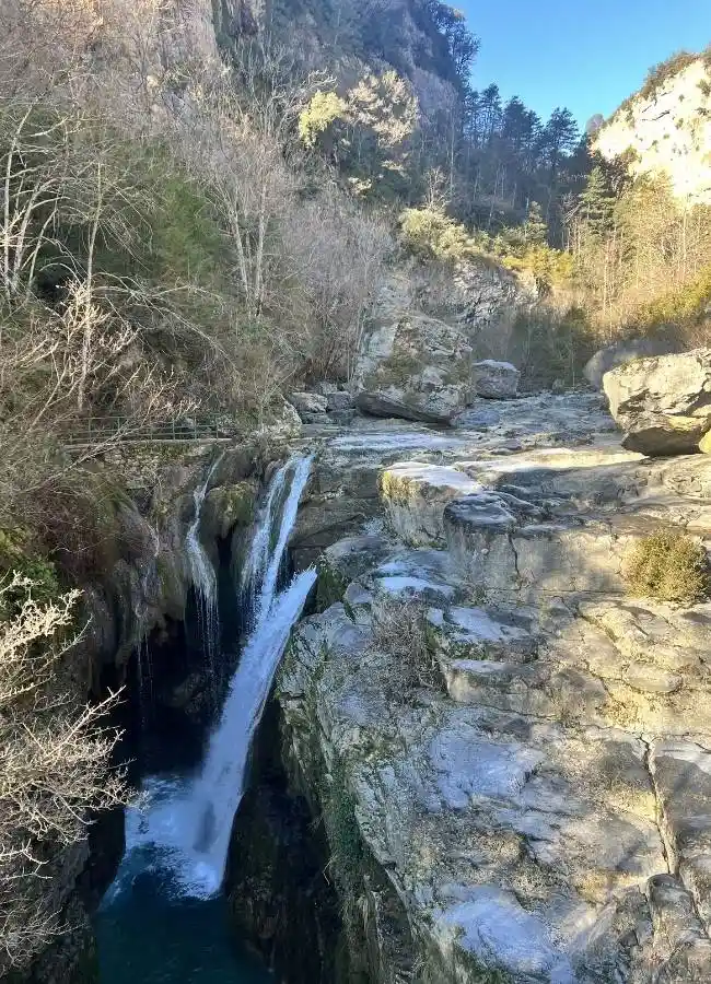 Impresionante cascada en cañón rocoso con árboles desnudos y montañas.