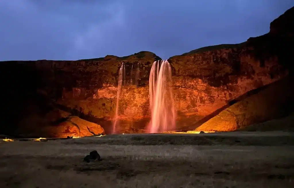 Cascada nocturna iluminada con tonos cálidos sobre acantilado.