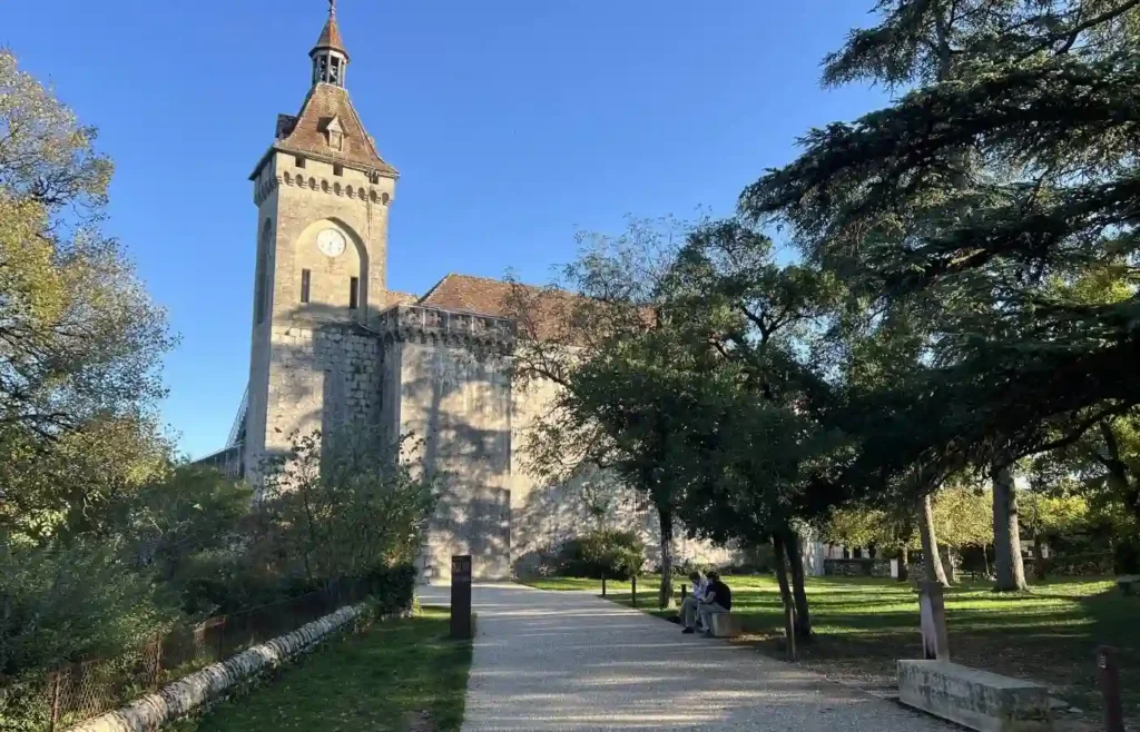 Torre medieval con reloj en un parque soleado con gente.