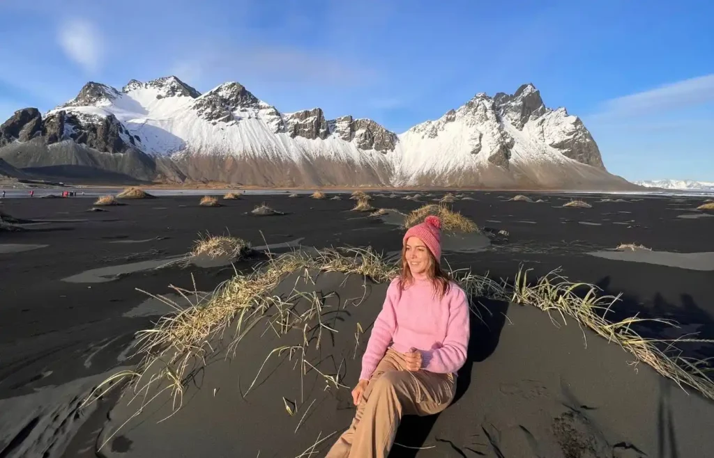 Mujer en dunas de arena negra con montañas nevadas en Islandia.