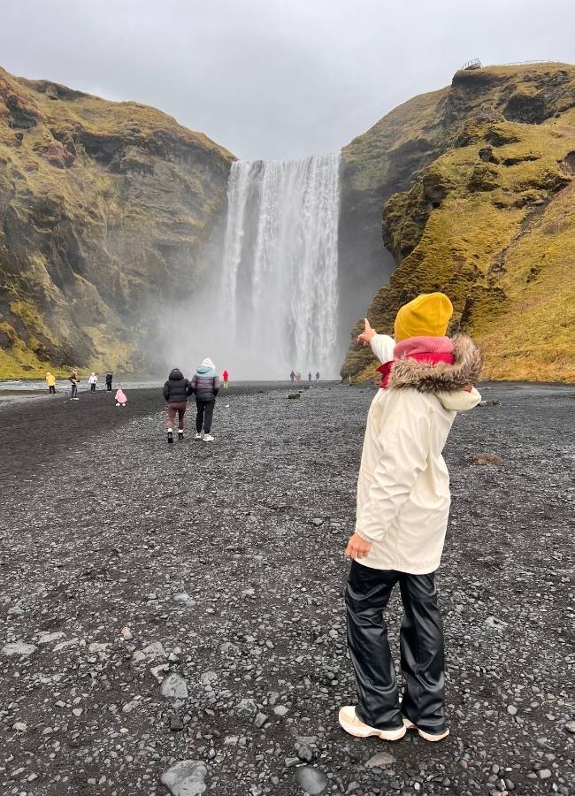 Viajera señalando la imponente caída de agua de la cascada Skógafoss en el sur de Islandia.