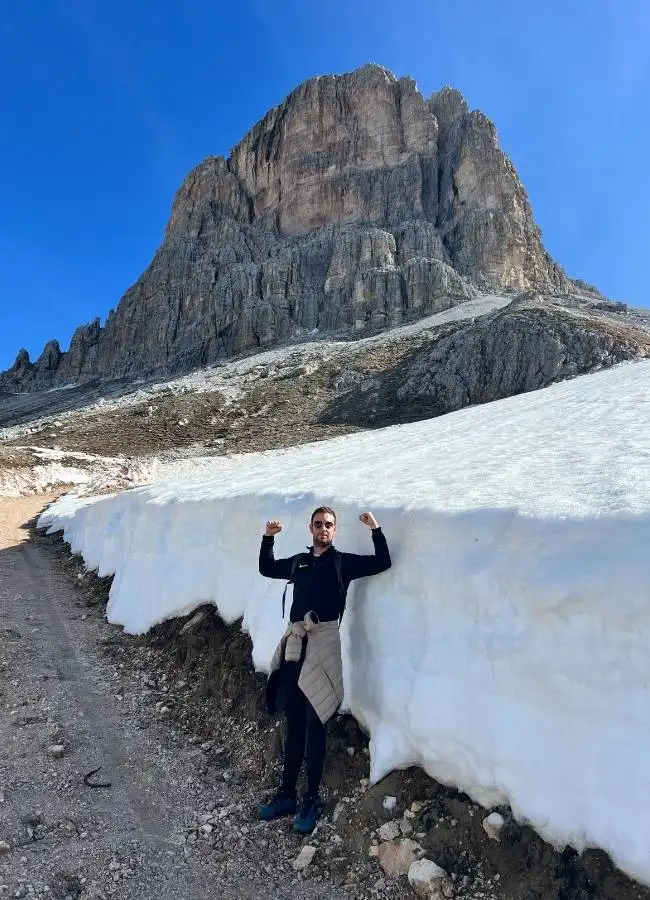 Hombre posando junto a muro de nieve con montaña de fondo.