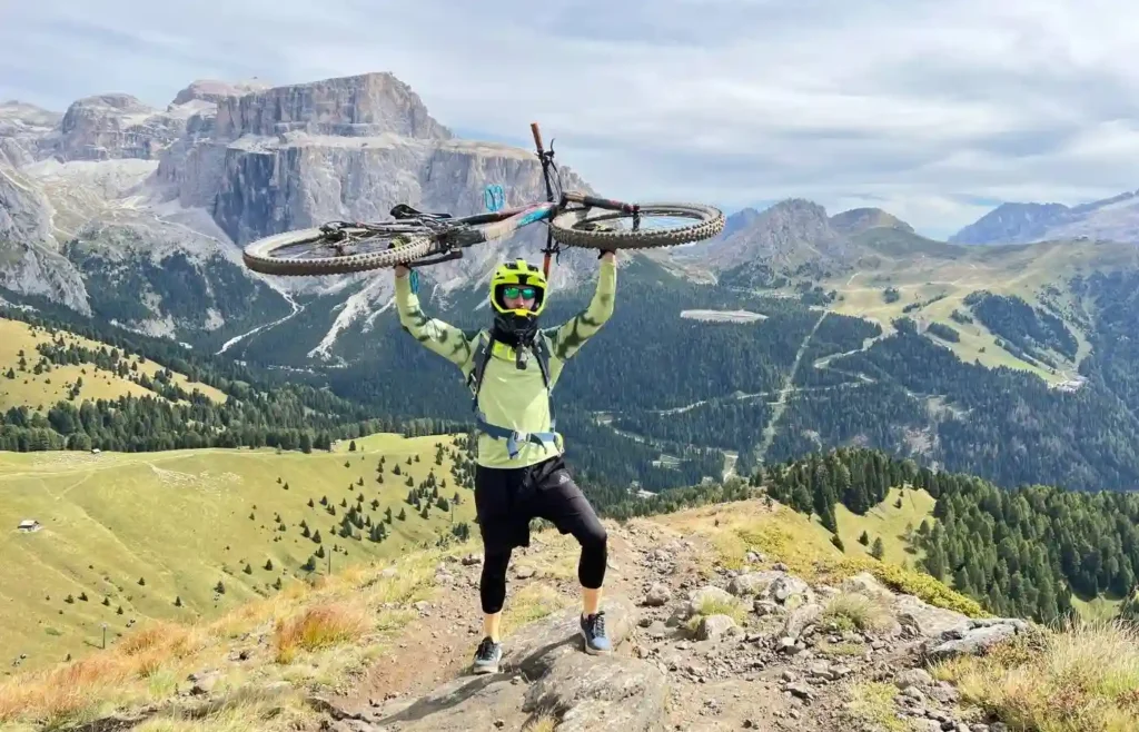 Ciclista de montaña victorioso con bici sobre la cabeza en los Dolomitas.