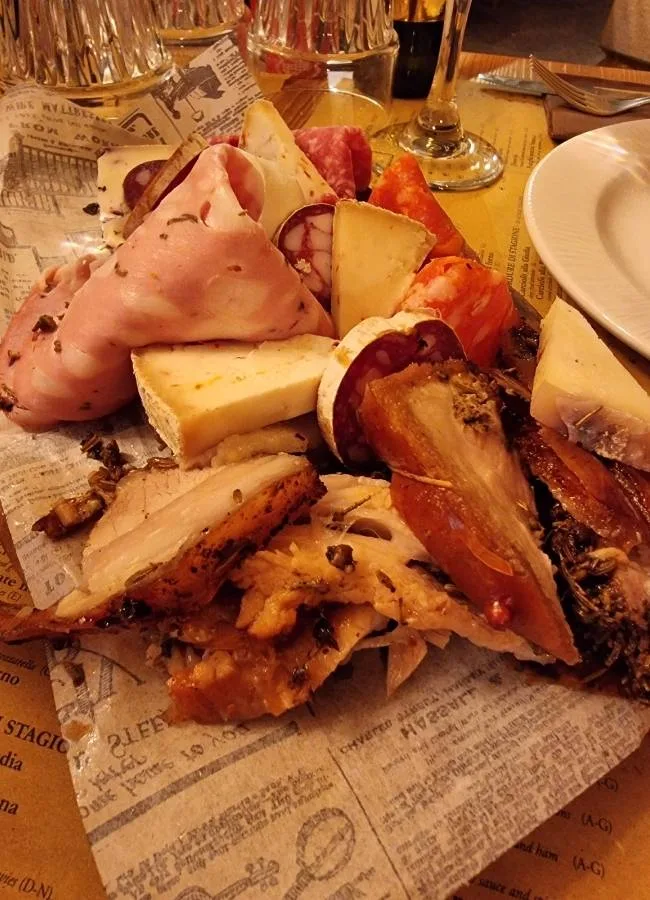 Una tabla tradicional italiana de embutidos, porchetta y quesos servida sobre papel de estraza en una taberna romana.