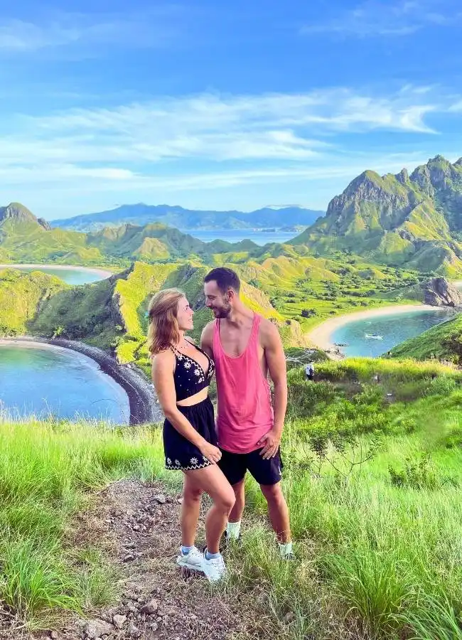 Pareja sonriente en cima montañosa con vistas impresionantes al mar.