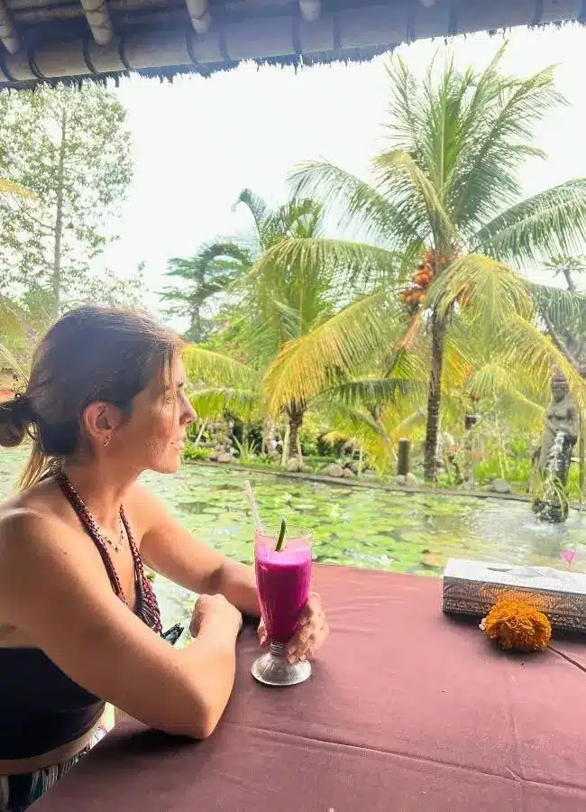 Mujer con bebida tropical, palmeras y estanque.