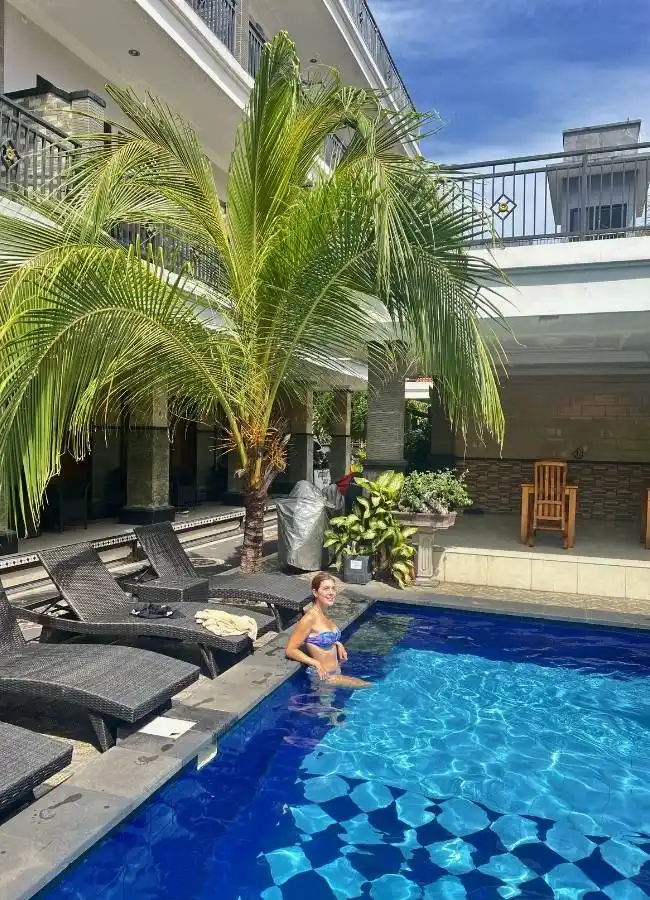 Mujer sonriente en bikini disfrutando de piscina con palmera.