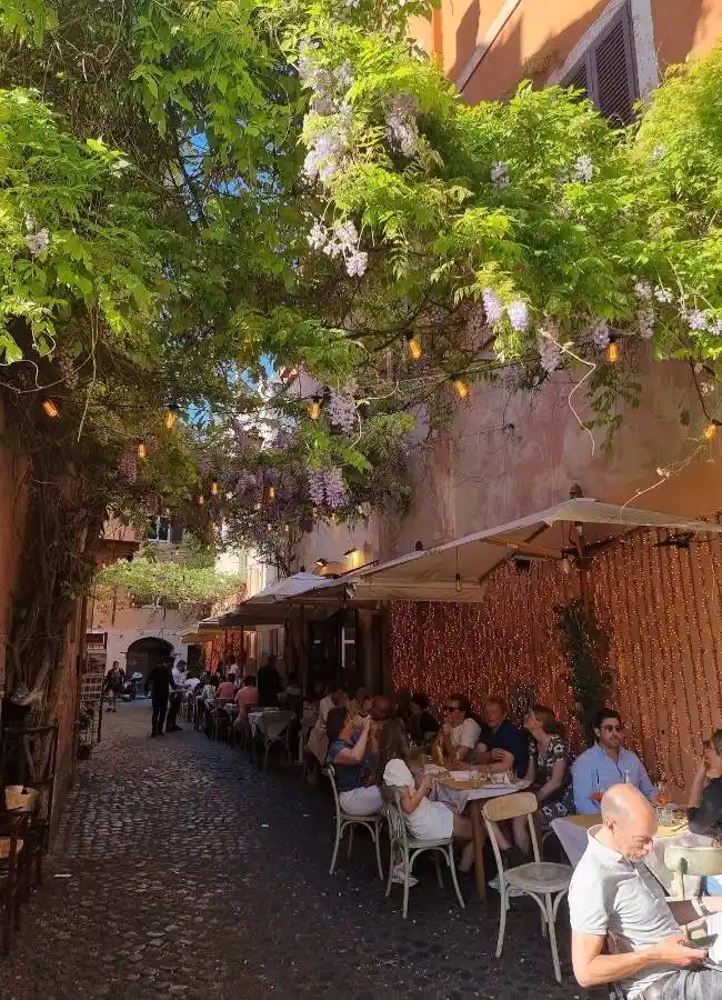 Ambiente de una encantadora terraza de un restaurante tradicional en un callejón arbolado del barrio de Trastévere.