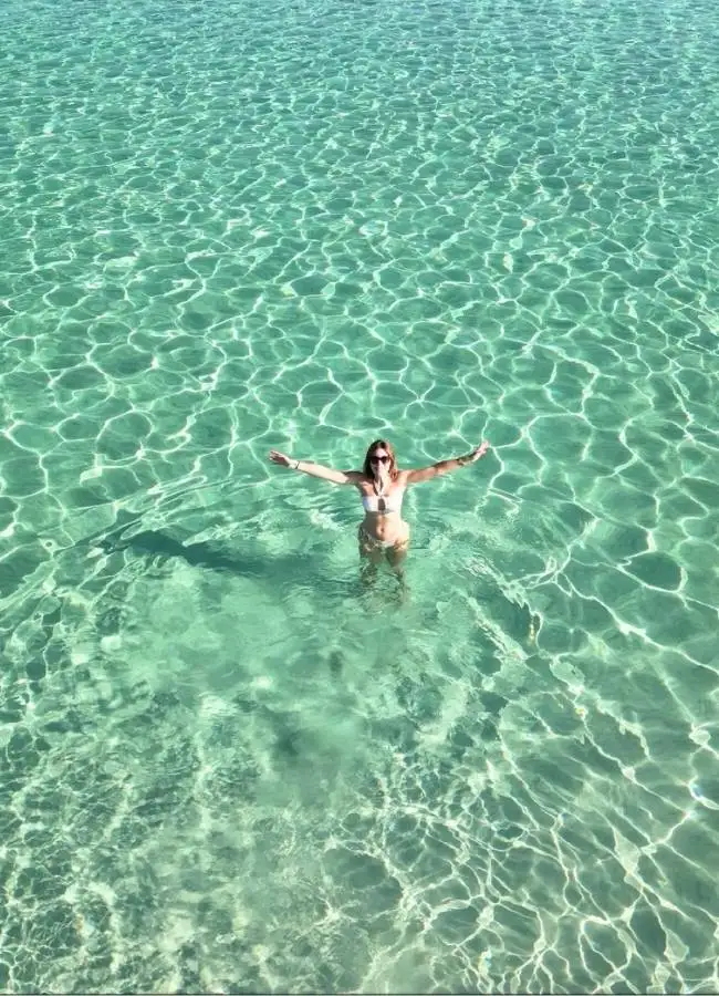 Vista aérea cenital de una persona nadando en las aguas caribeñas de una playa de Cerdeña.