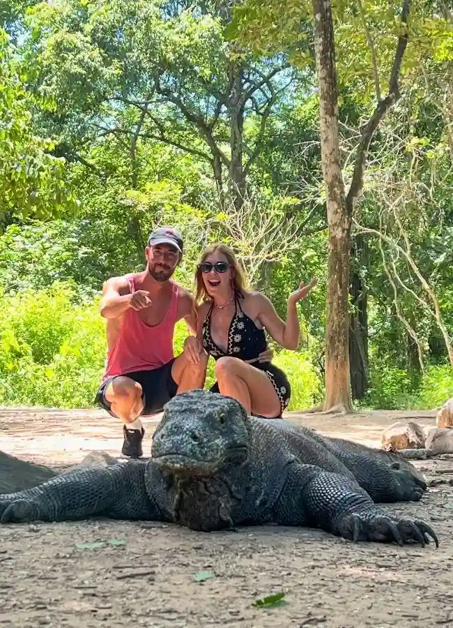 Pareja posando felizmente con un dragón de Komodo en la naturaleza.