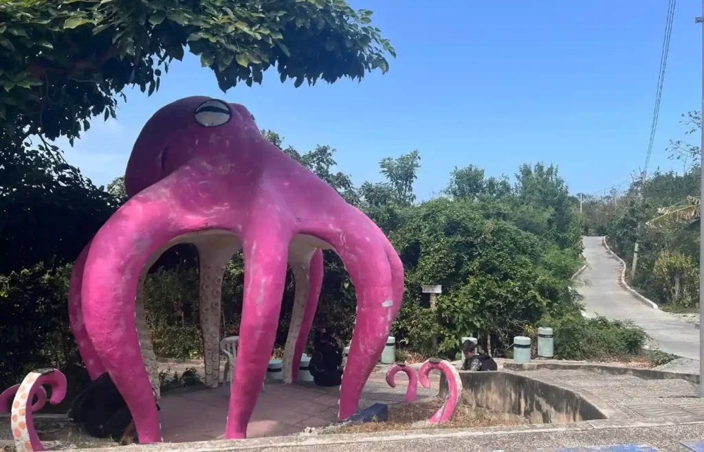 Escultura de pulpo rosa gigante al aire libre bajo cielo azul.