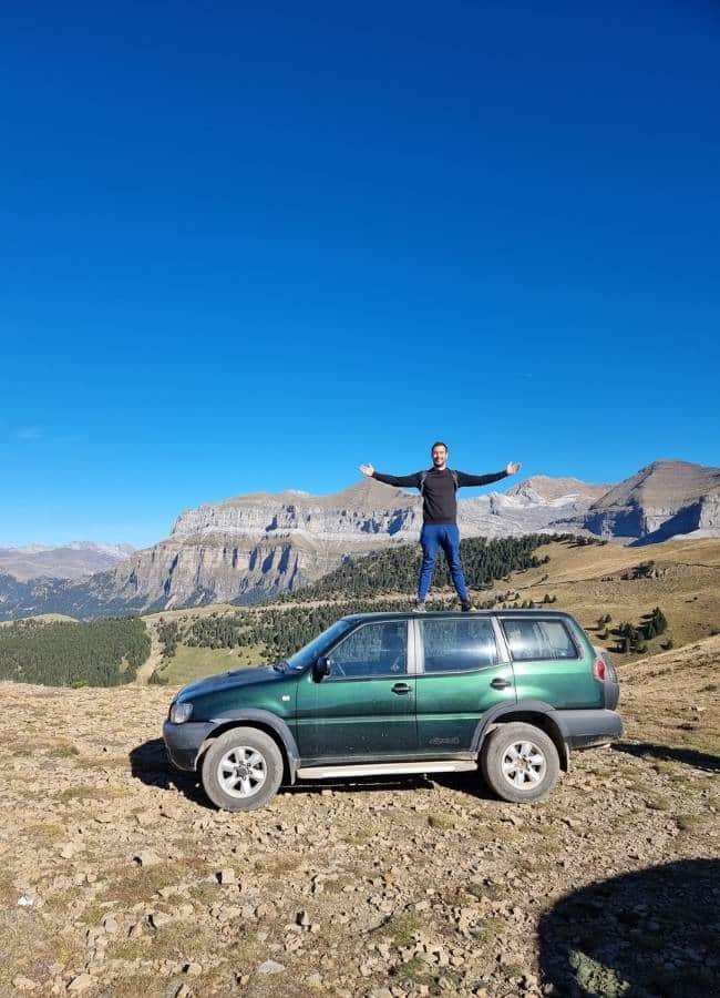 Hombre feliz sobre todoterreno en montaña bajo cielo azul.