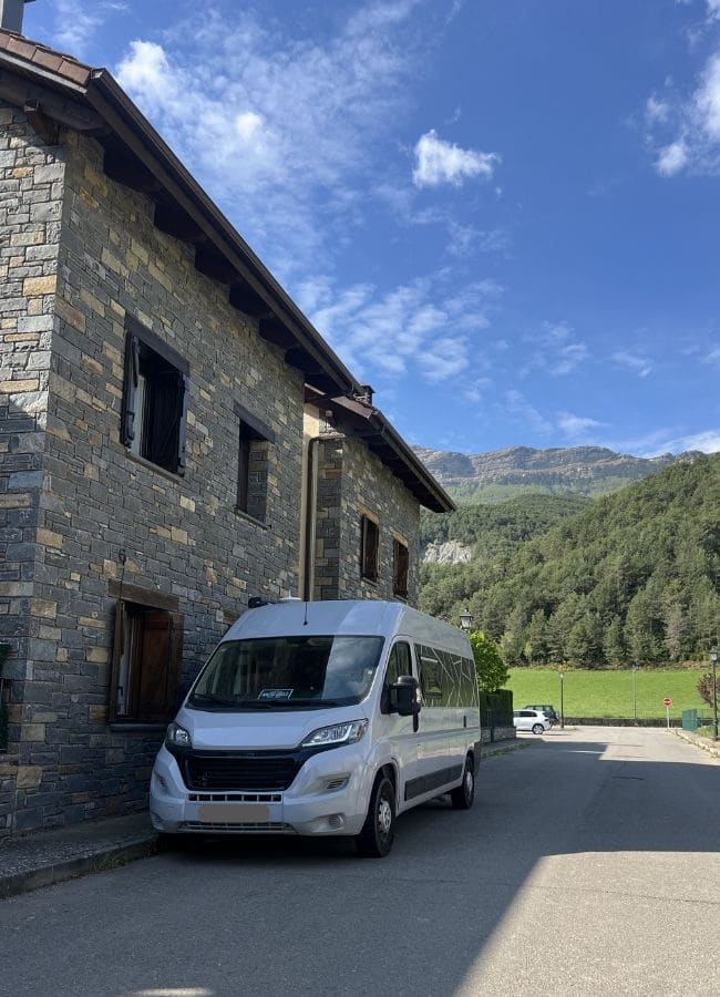 Furgoneta camper estacionada frente a una casa de piedra tradicional en el pueblo de Fiscal.