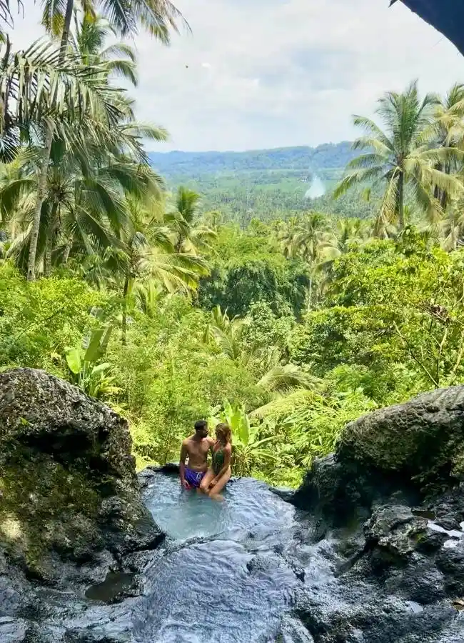 Pareja en piscina natural con vistas a selva tropical.