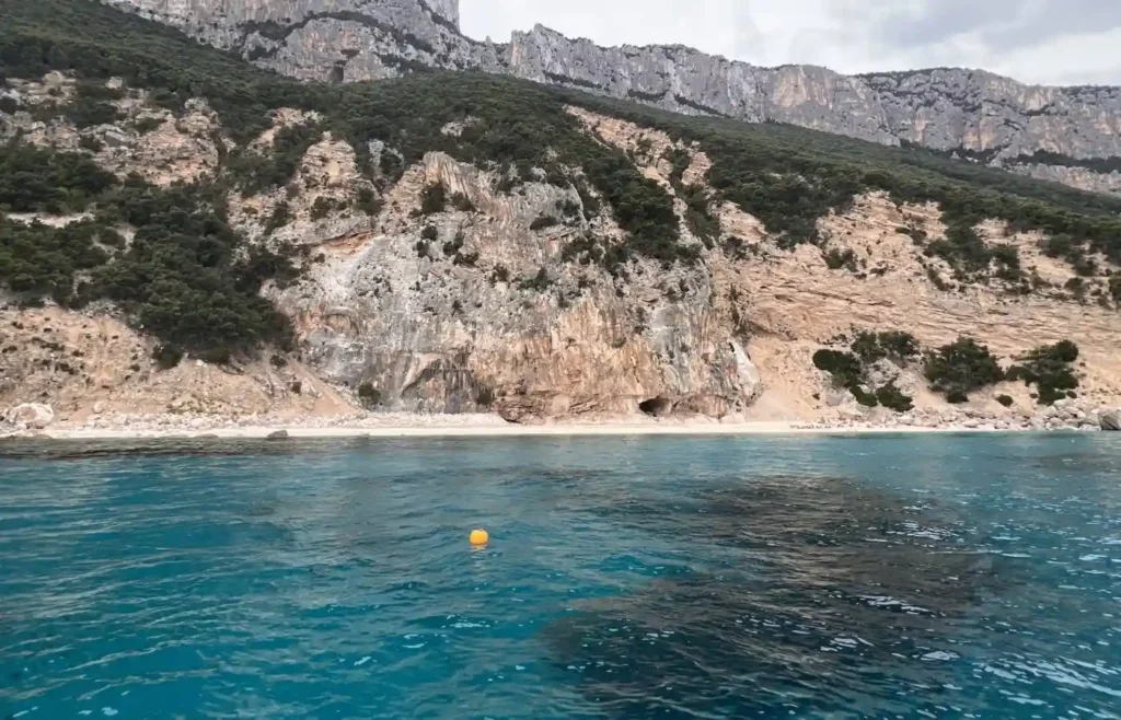 Playa virgen con acantilados, mar turquesa y boya naranja.