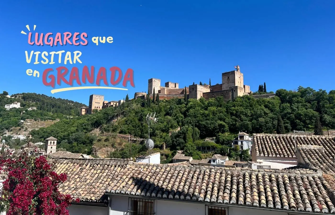 Imagen de portada de la guía "Lugares que visitar en Granada", mostrando una panorámica de la Alhambra desde el Albaicín con tejados y buganvillas en primer plano.