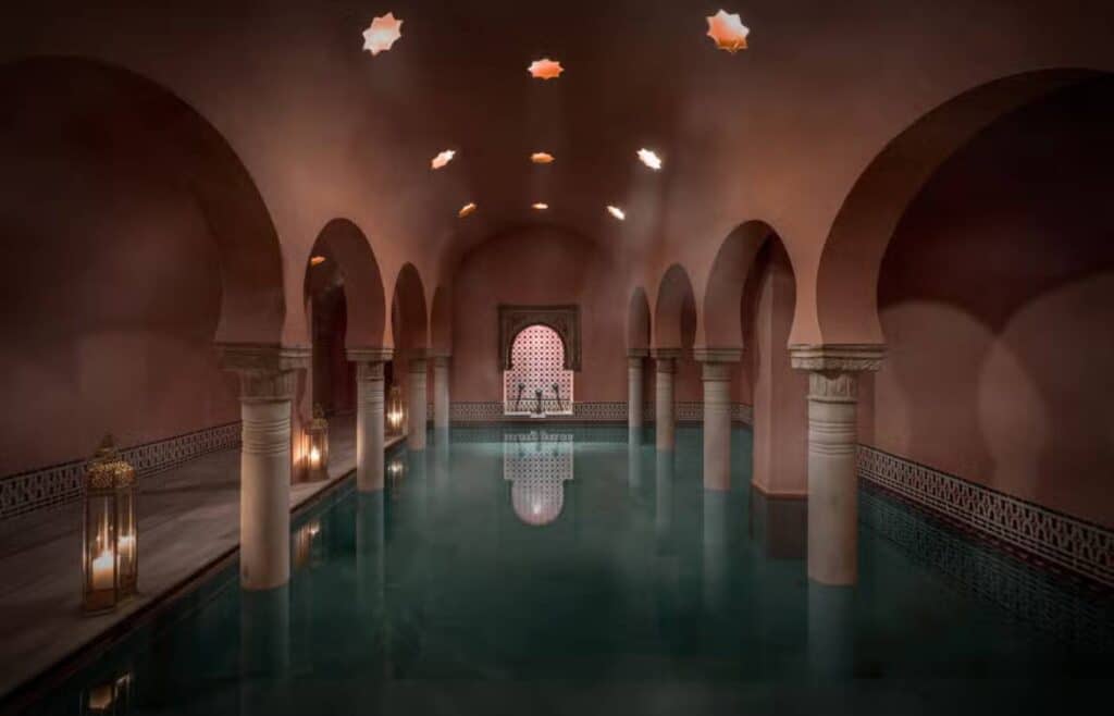Piscina interior de un hammam con luz tenue, arcos de herradura y tragaluces en forma de estrella.