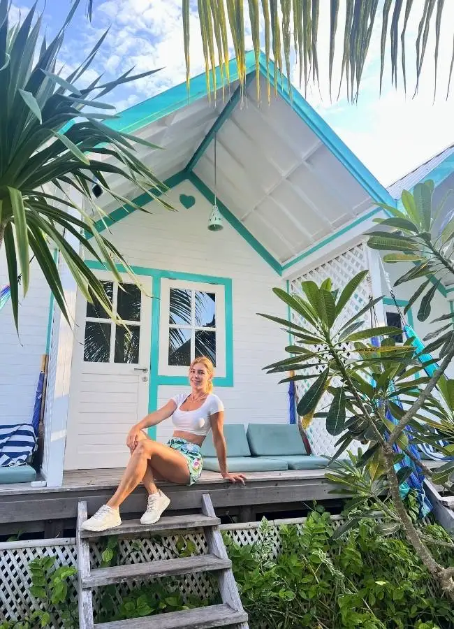 Viajera sentada en las escaleras de madera de un bungalow blanco y turquesa en Le Pirate Gili Meno.