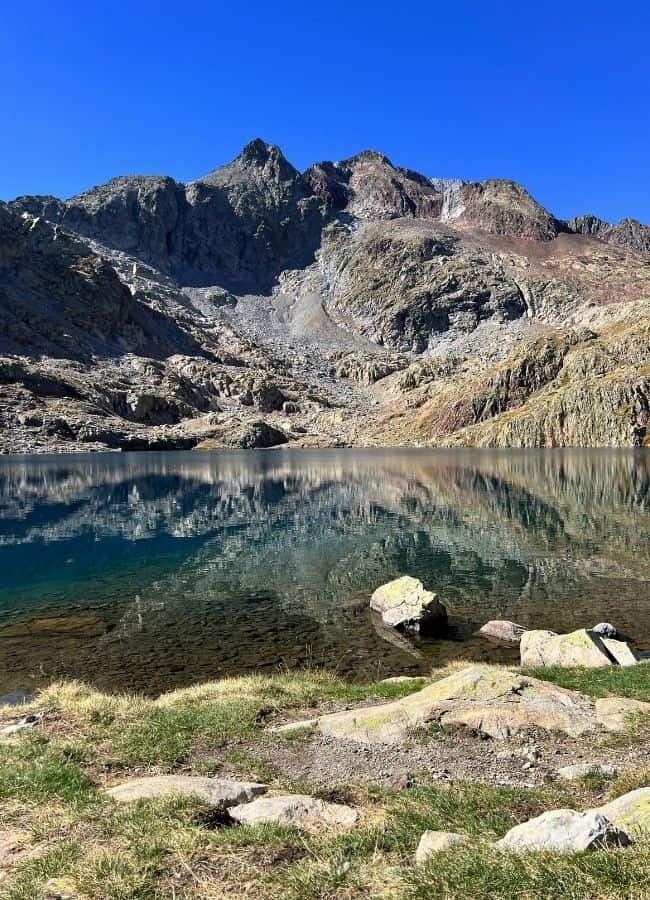Reflejo de las montañas rocosas en el agua azul de un ibón de alta montaña en el Pirineo Aragonés.