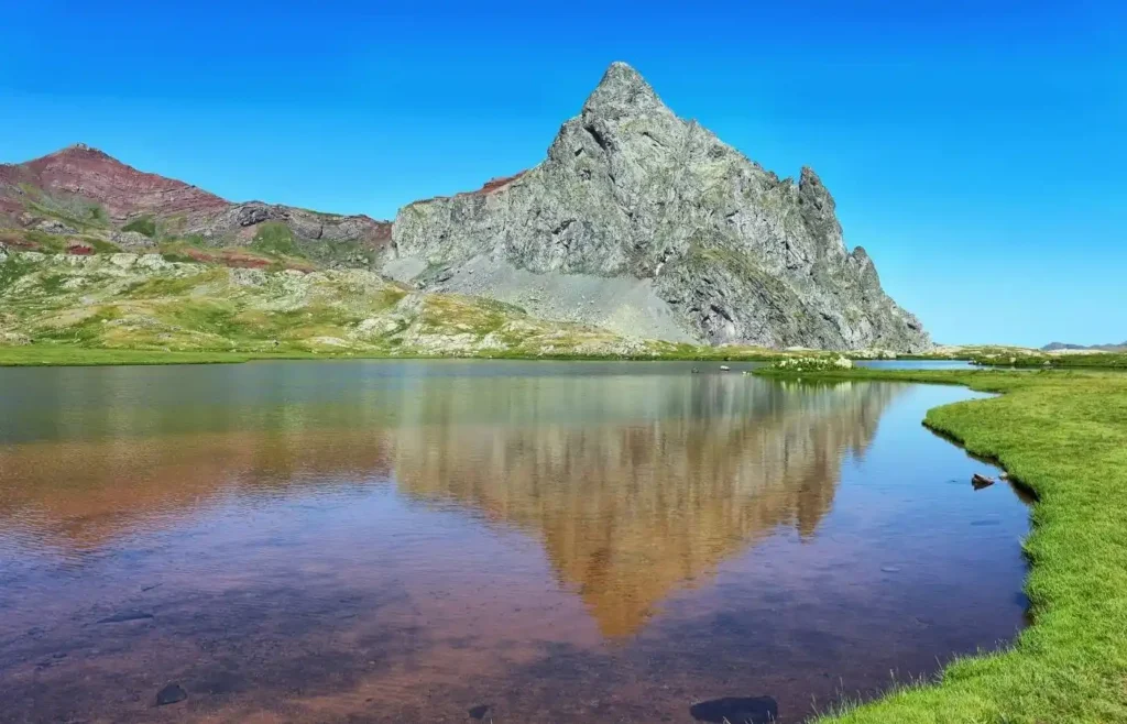 Pico montañoso reflejado en lago bajo cielo azul.