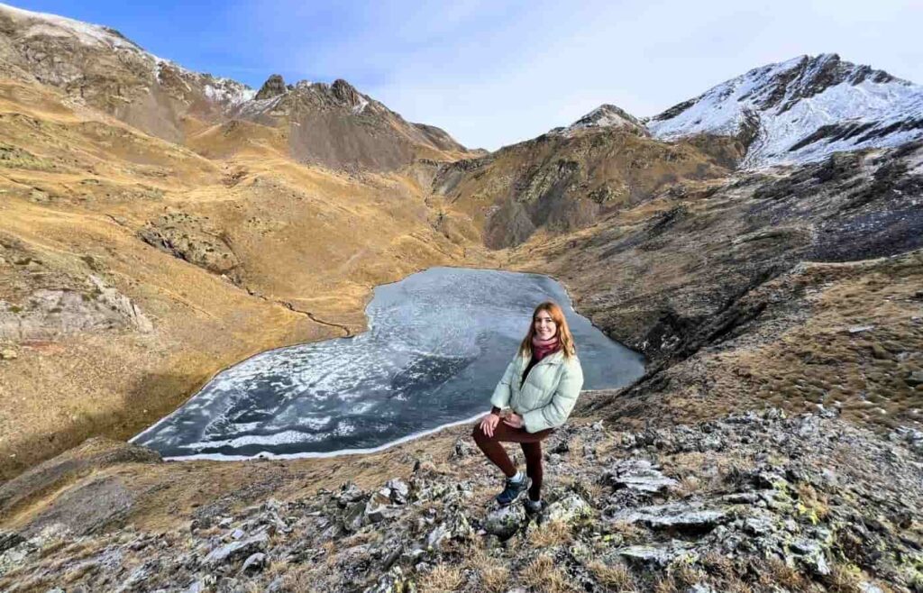 Mujer posando frente al Ibón de Catieras parcialmente helado en invierno.