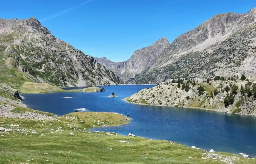 Lago de montaña azul, picos rocosos y cielo claro.