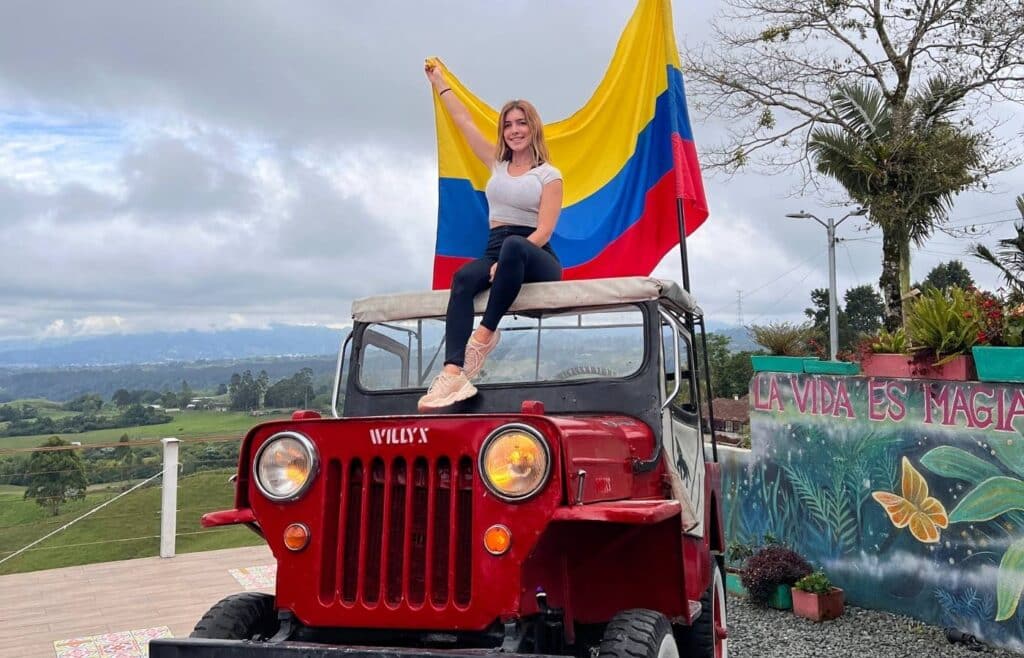 Chica posando sobre un Jeep Willys rojo con la bandera de Colombia en el Eje Cafetero.