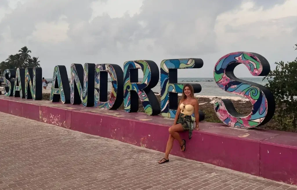 Mujer sonriente en letras SAN ANDRÉS junto al mar.