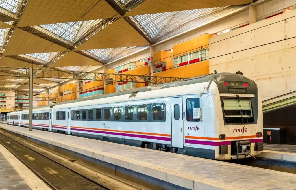Tren Renfe en andén de estación moderna con techo acristalado.