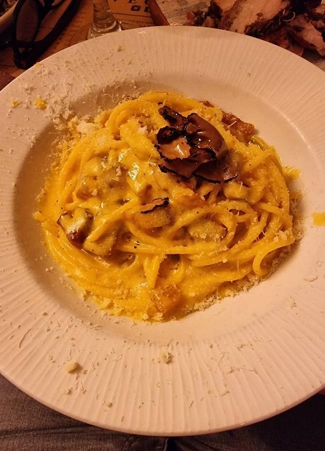 Pasta cremosa con trufa negra y queso rallado en plato blanco.