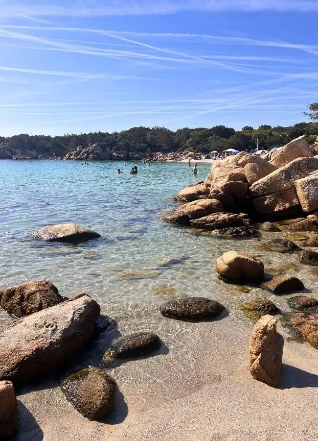Cala de arena fina rodeada de grandes bloques de piedra redondeados en el litoral de Cerdeña.