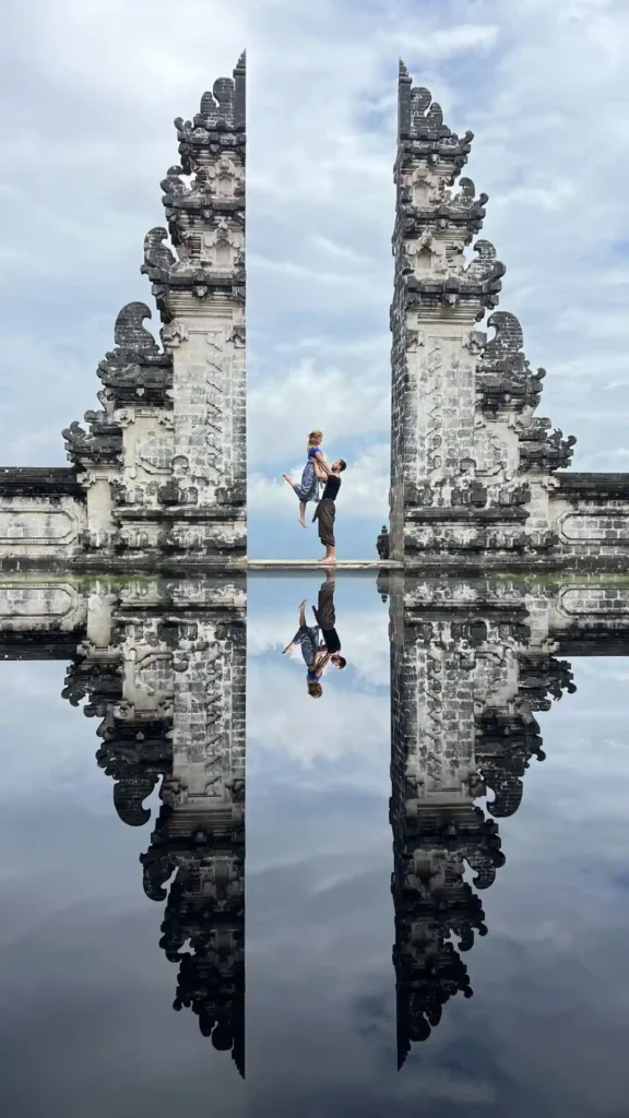 Pareja posando de espaldas entre las puertas de piedra de Pura Lempuyang con el reflejo simétrico en Bali.