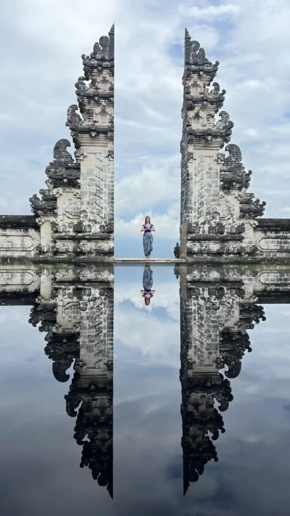 Mujer en puerta de templo balinés reflejada en agua.