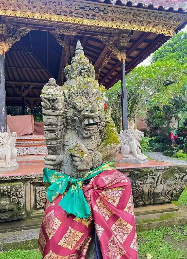 Estatua de piedra con vestimenta tradicional sarong en la entrada de un templo balinés.