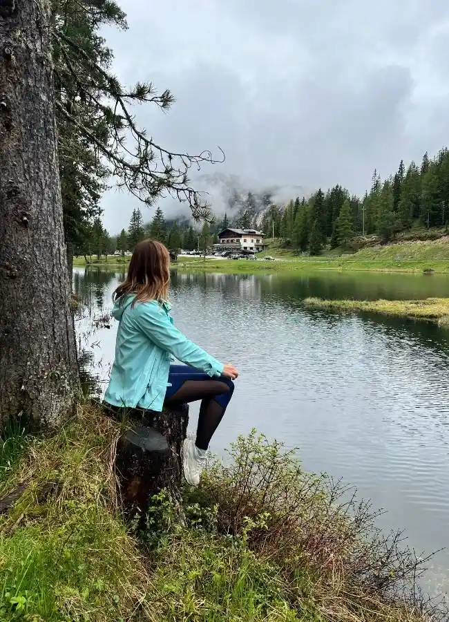Mujer sentada junto al lago, paisaje montañoso con niebla.