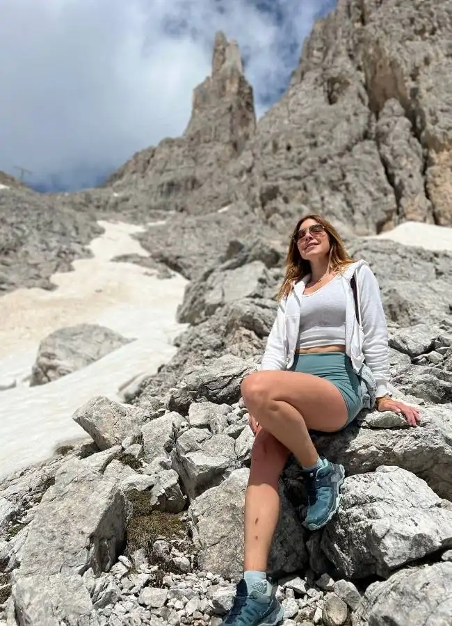 Mujer sonriente descansando en rocas de montaña nevada.