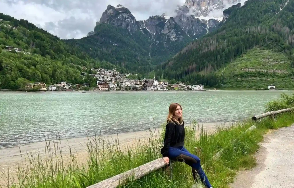 Mujer en lago de montaña, pueblo y Dolomitas.