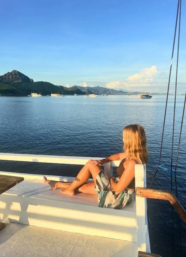 Mujer relajada en barco mirando el mar y montañas.