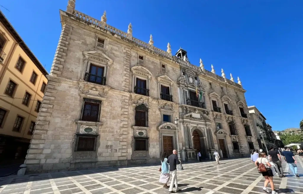 Fachada de piedra labrada del Palacio de la Madraza en una plaza concurrida de Granada.